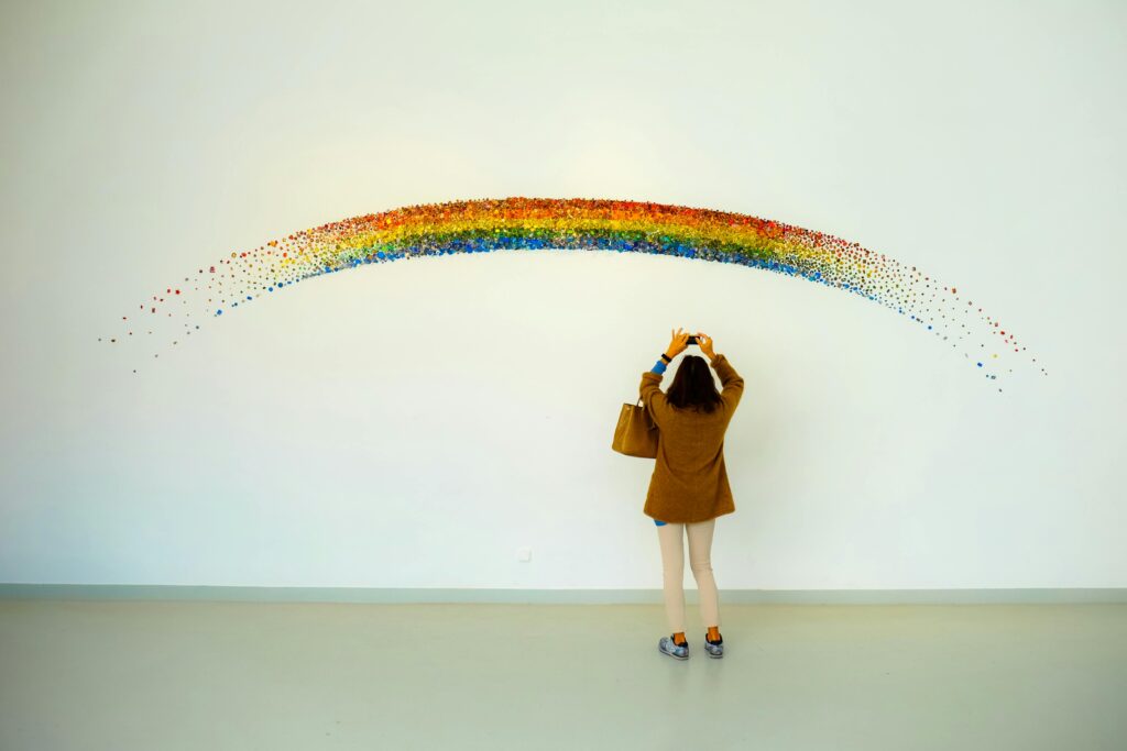 A woman stands observing a colorful rainbow art installation indoors.