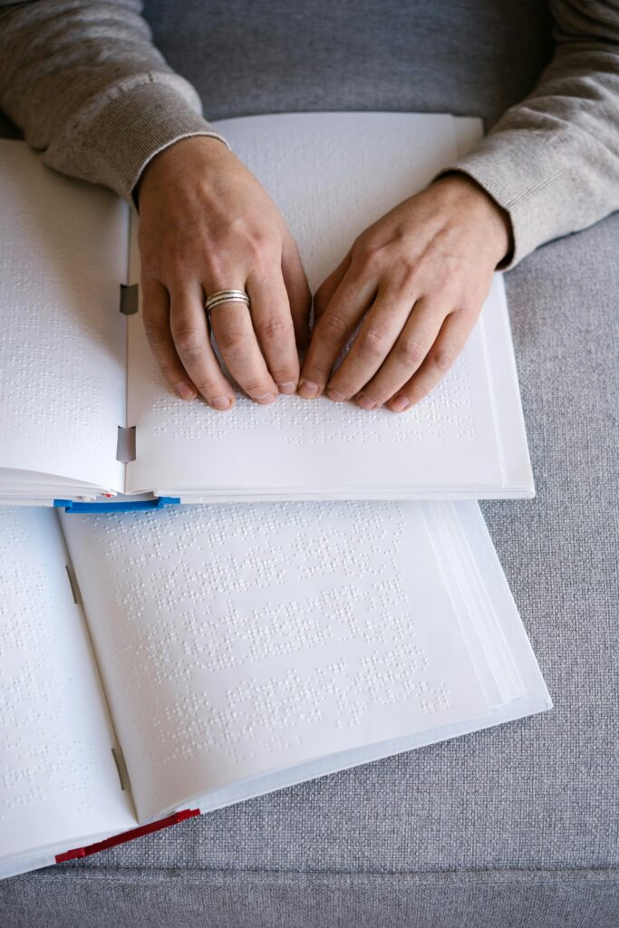 Hands reading Braille text on an open book, representing tactile reading and accessibility.