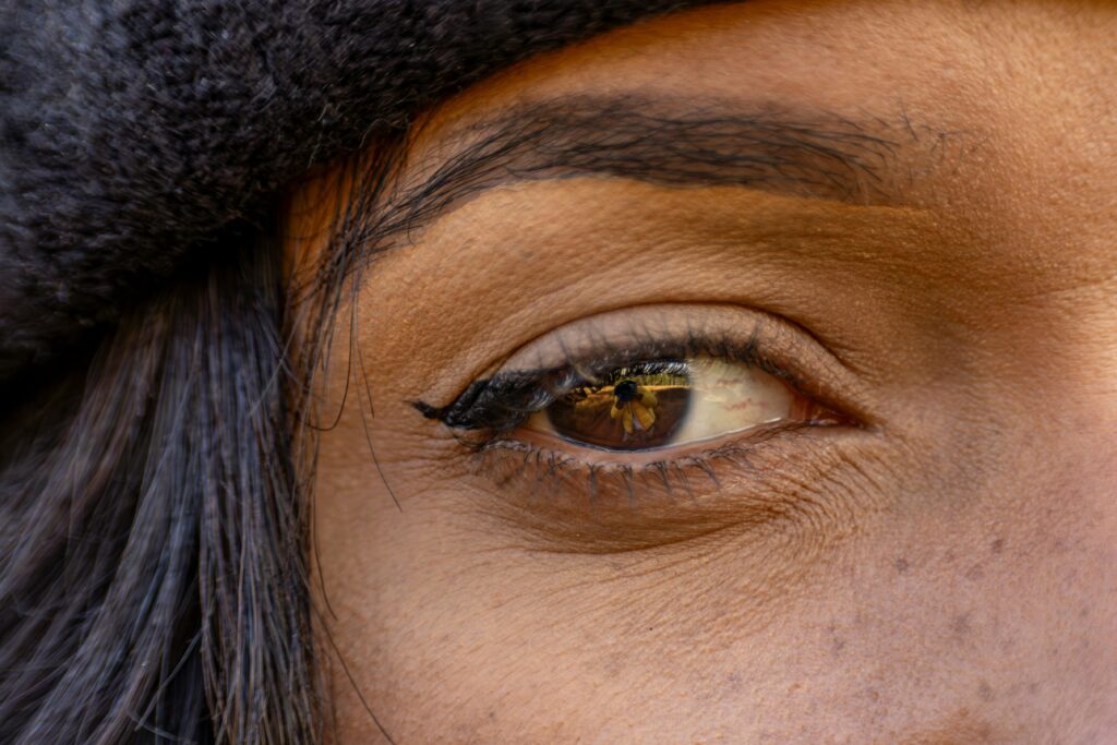 Detailed close-up of an eye with eyeliner, wearing a warm hat, reflecting a scene.