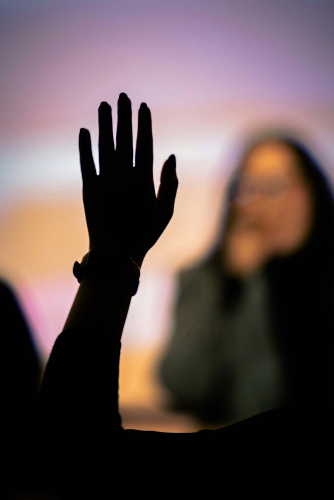 Silhouetted hand raised during a presentation, blurred speaker in the background.