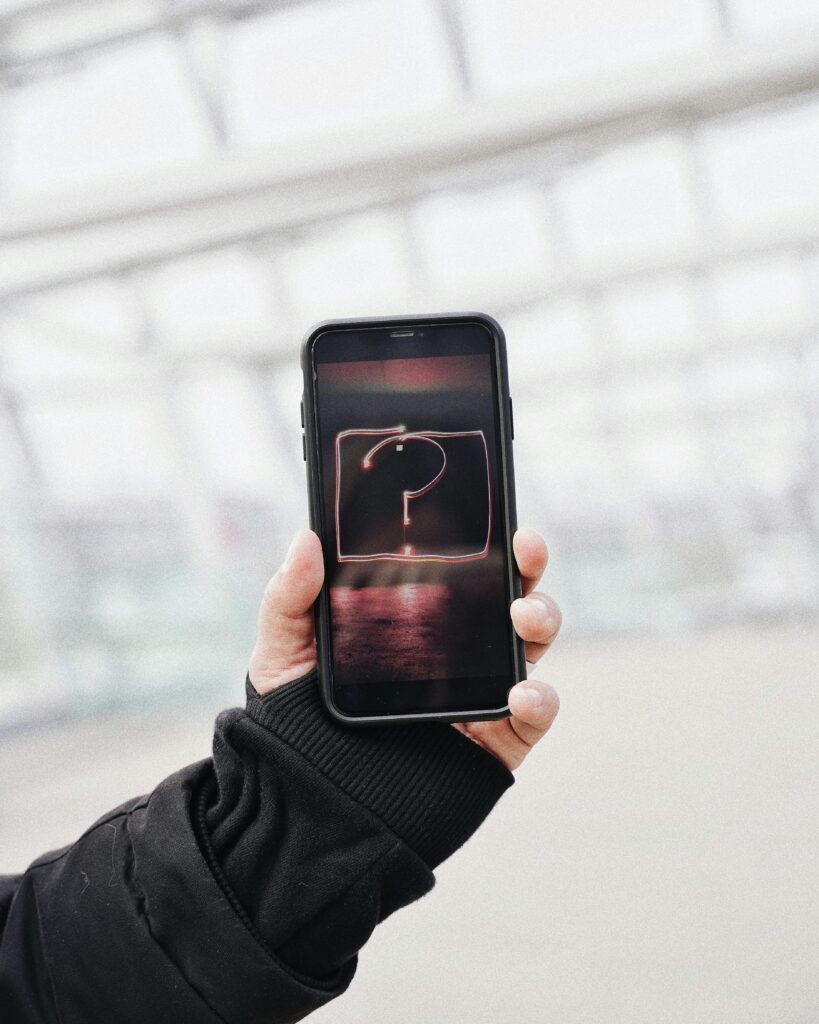 Close-up of a hand holding a smartphone showing a glowing question mark, symbolizing inquiry and technology.