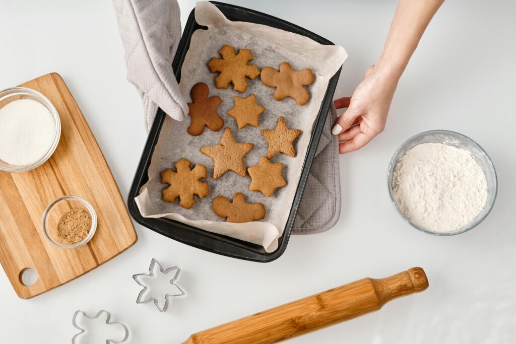 Overhead view of gingerbread cookies on a baking tray with ingredients and cookie cutters.