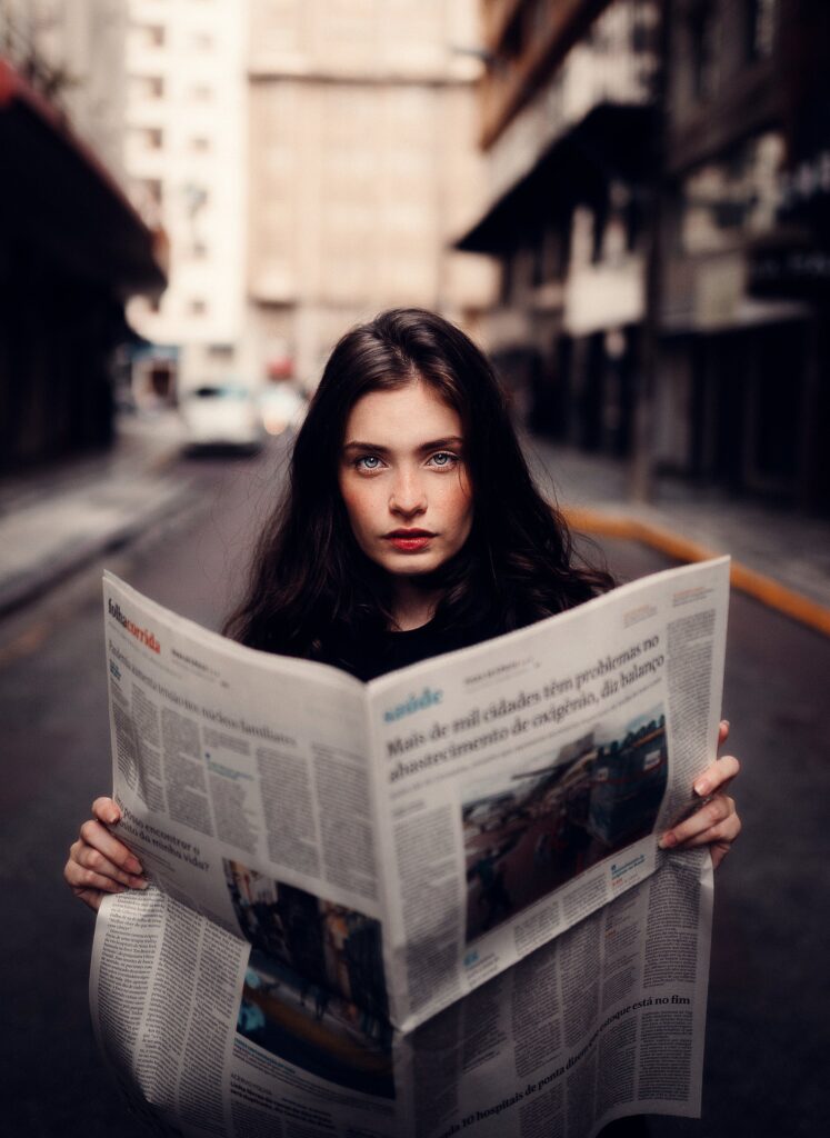 Portrait of a woman standing in an urban street holding a newspaper.