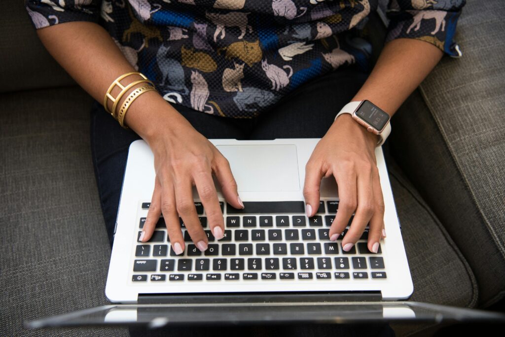 Close-up of a woman's hands typing on a laptop with an Apple Watch and bracelets.