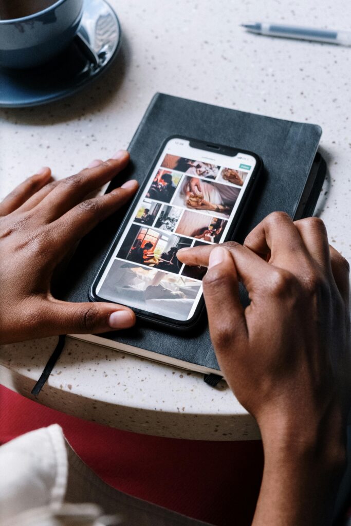 A person uses a smartphone to browse social media while sitting at a cafe table, coffee cup nearby.