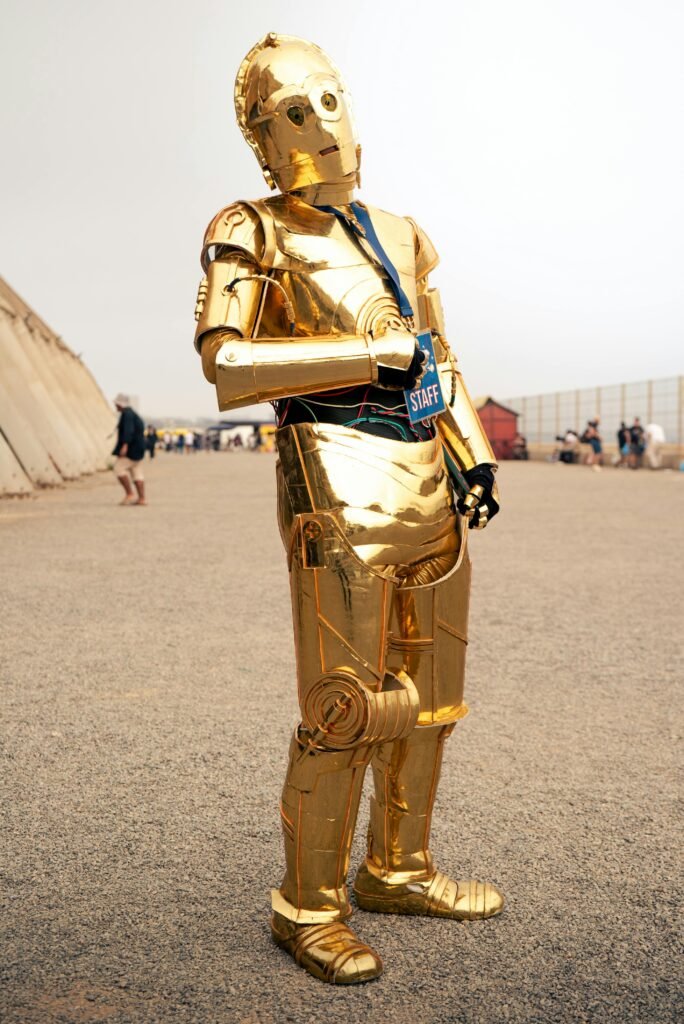 A gold-colored robot character dressed as staff at an outdoor event.