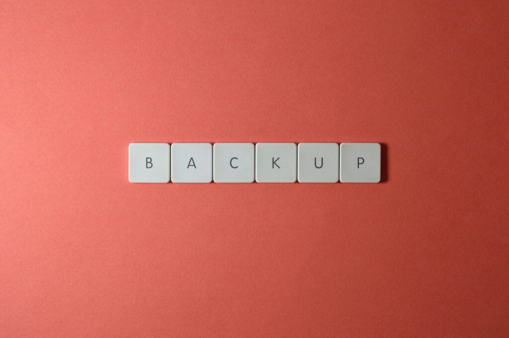 Close-up of keyboard keys spelling 'BACKUP' placed on a coral-colored surface.